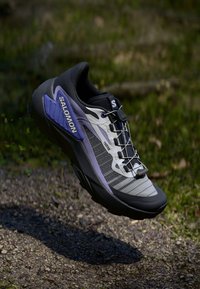 Běžecká obuv Salomon na trail s šedým a černým síťovaným svrškem a fialovými akcenty, texturovanou podešví a aerodynamickým designem pro venkovní použití.