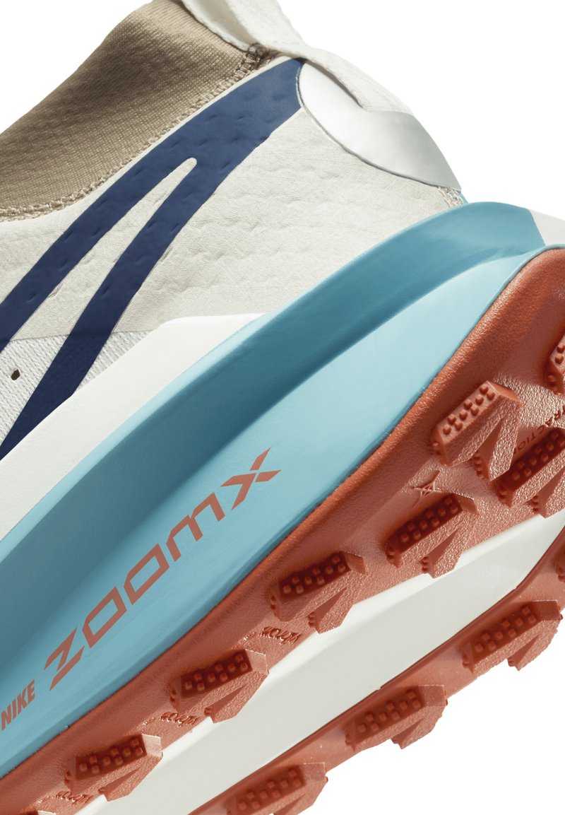 Scarpa da corsa con una tomaia bianca texturizzata, dettagli beige, una intersuola blu e una suola arancione con tacchetti di trazione marcati.