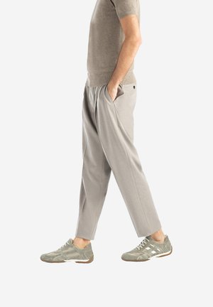 Grå, løstsiddende bukser med en tekstureret finish, der har en elasticeret talje og sidelommer, kombineret med grøn-grå sneakers.