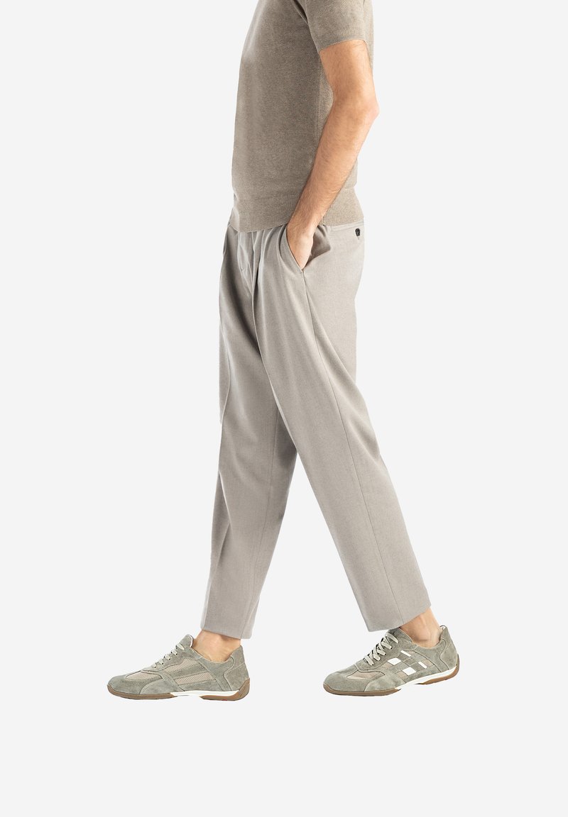 Šedé, volné kalhoty s texturovaným povrchem, mají pružný pas a postranní kapsy, doplněné zelenošedými teniskami.