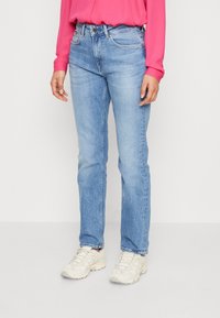 Vaqueros de pierna recta en azul claro con ligero desgastado. Cuenta con cinco bolsillos y costuras sutiles. Combinado con una blusa rosa y zapatillas deportivas ligeras.