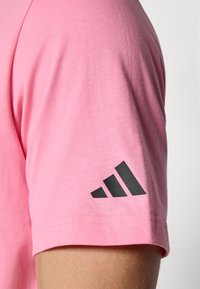 Pink cotton t-shirt featuring a black three-stripe logo on the sleeve. The fabric has a smooth texture and a classic fit.