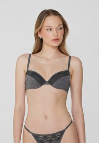 Soutien-gorge gris et string assorti avec une texture de tissu lisse et des accents en dentelle. Conception à armatures avec bretelles réglables.