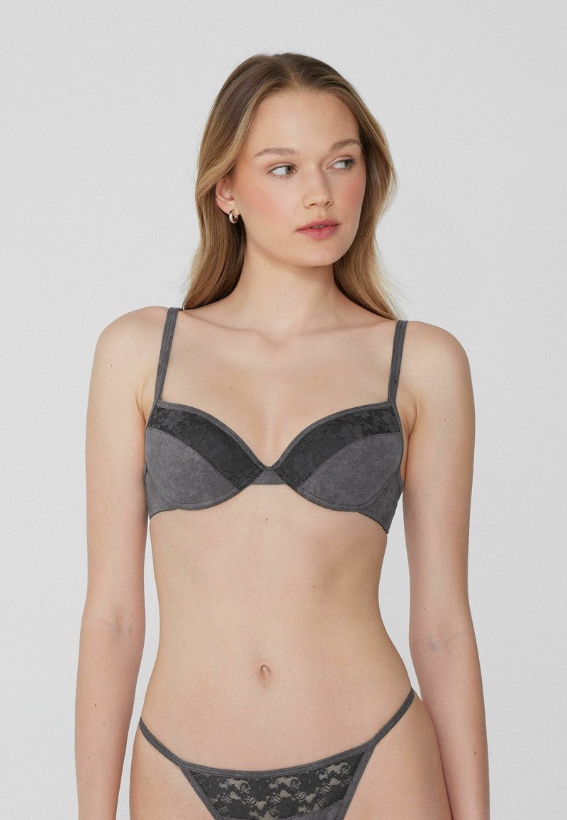 Soutien-gorge gris et string assorti avec une texture de tissu lisse et des accents en dentelle. Conception à armatures avec bretelles réglables.
