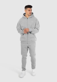 Gray zip-up hoodie with a spacious hood and elastic cuffs, paired with matching gray sweatpants. Both are made of soft, textured material.