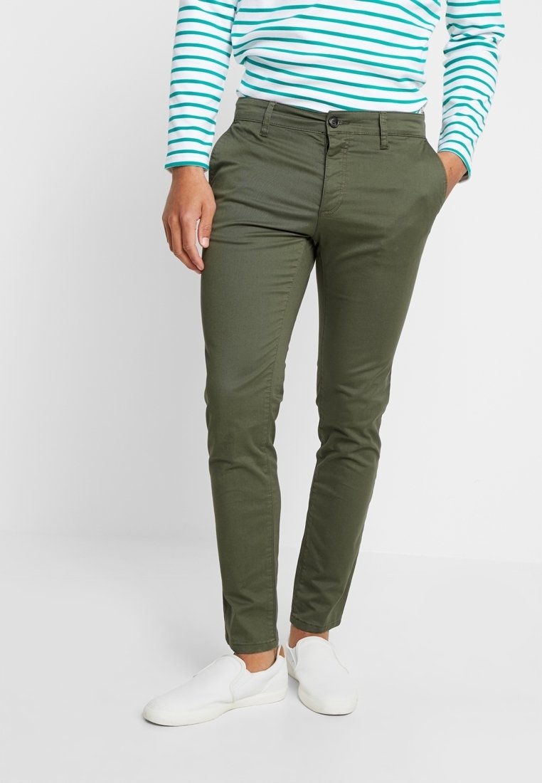 Oliwkowozielone, dopasowane spodnie z gładkiej tkaniny, z przednimi kieszeniami, zamkiem błyskawicznym i zapięciem na guzik. Noszone z pasiastą bluzką i butami.