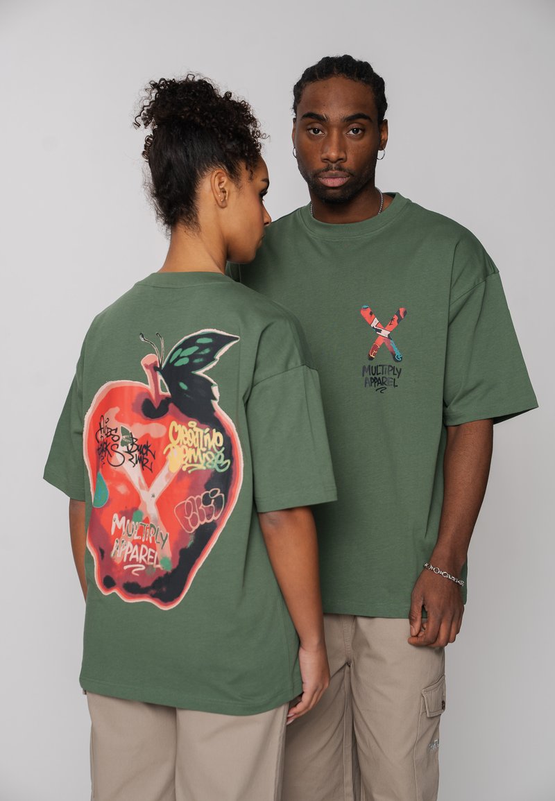 Deux mannequins portent des t-shirts oversize vert olive avec des imprimés graphiques colorés "Multiply Apparel", l'un montrant le design avant et l'autre le design arrière.
