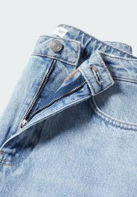 Jean en denim bleu clair avec braguette zippée et fermeture par bouton métallique. Tissu légèrement usé et détails de couture visibles.