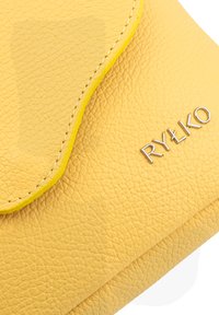 Clutch gialla in pelle con superficie texturizzata, patta arrotondata, cuciture gialle a contrasto e logo argento "RYŁKO" sul fronte.