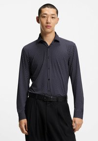 Camicia navy a maniche lunghe con pois bianchi e colletto a punta. Indossata con pantaloni neri e una cintura, con una vestibilità su misura.