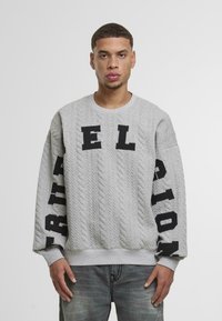 Hanorac tricotat gri cu un model texturat de cabluri, cu litere negre îndrăznețe care spun "EL" pe piept și "RION" pe mâneci. Textură moale.