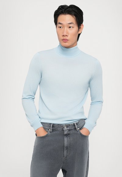 Lyseblå turtleneck-genser i mykt strikkemateriale, med lange ermer og en tettsittende silhuett, kombinert med grå high-waisted jeans.
