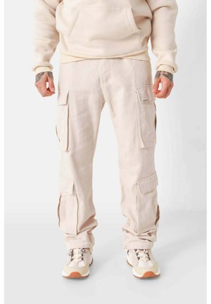 Beige cargobroek van katoen met meerdere zakken, een ontspannen pasvorm en opgerolde broekspijpen, gecombineerd met lichtgekleurde sneakers.