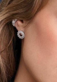 Silverörhängen med en cirkulär design som har små klara stenar, vilket skapar en texturerad yta runt ett centralt öppet hål.