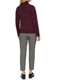 Bordeaux pullover trui met hoge kraag, gecombineerd met grijze taps toelopende broek; gladde textuur en aansluitend ontwerp; zwarte instappers zichtbaar.