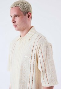 Lichtgele T-shirt met korte mouwen, voorzien van een gehaakt patroon, casual kraag en een kleine borstzak met een metalen accent.