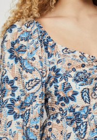 Rochie florală cu un fundal crem și modele botanice albastre și maronii. Material texturat cu mâneci bufante și decolteu pătrat.