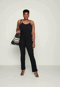 Top preto de alças, combinado com calças pretas de cintura alta. Inclui uma mala de tote em preto e creme com padrão e sandálias pretas de tiras.