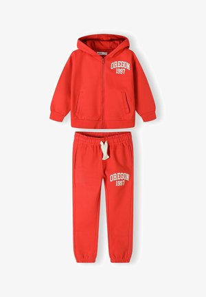 Survêtement en coton rouge avec un hoodie zippé et un pantalon à cordons. Présente l'inscription "OREGON 1997" imprimée en blanc sur les deux pièces. Texture lisse.