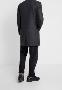 Mørkegrå lang blazer med en skræddersyet pasform og en central rygslids, parret med sorte bukser og sorte sneakers med hvide accenter.