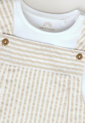 Salopette rayée beige et blanche avec détails en boutons et une chemise intérieure blanche. Matériau en coton doux au toucher lisse. Logo NEXTbaby visible.