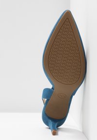 Chaussure à talon haut en daim bleu avec bout pointu et talon fin. Semelle en caoutchouc marron avec motif texturé, comportant le logo "MK".