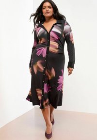 Schwarzes Hemdkleid mit langen Ärmeln, das mit einem floralem Druck in rosa und lila Tönen versehen ist. Glatte Stoff, knielang, taillierter Schnitt.