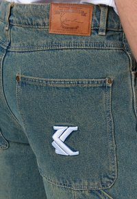 Traperice u izblijedjelo plavoj boji s kožnom etiketom i izvezenom logotipom na stražnjem džepu. Imaju dvostruko šivanje i metalne dodatke.