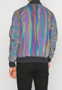 Irydyscencyjna kurtka bomberka z prążkowanym kołnierzem i mankietami. Posiada długie rękawy i elastyczny pas. Materiał ma błyszczącą, odblaskową fakturę.