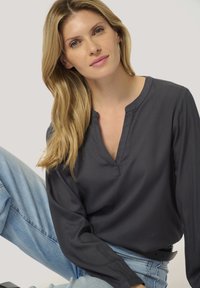 Dark grey, long-sleeve top with a relaxed fit and a V-shaped neckline. Smooth fabric and minimal seams complement light blue jeans.
