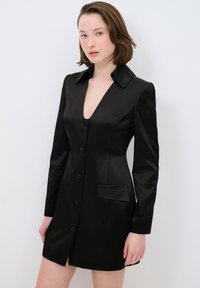 Schwarzes Satin-Kleid mit V-Ausschnitt, langen Ärmeln, Knopfleiste und einer einzigen Tasche. Verfügt über einen strukturierten Kragen und eine taillierte Silhouette.