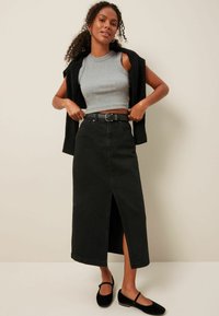 Melna denima maksi svārki ar priekšējo šķēlumu, saskaņota ar pieguļošu pelēku crop top un melnu cardigan. Modelis valkā melnu jostu un atbilstošas kurpes.