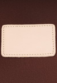 Bež pravokutni kožni flaster s vidljivim šavovima na tamnoljubičastoj pozadini od tkanine.