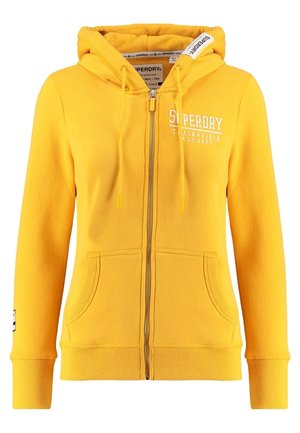 Sweat à capuche jaune zippé avec poches avant, capuche avec cordon de serrage et logo blanc "Superdry Track & Field Ath. Dept" sur la poitrine et l'étiquette de la capuche.