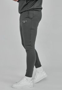 Pantaloni della tuta grigi a vestibilità slim, con tasche frontali e dettagli in logo bianco, abbinati a sneaker bianche e polsini a coste.