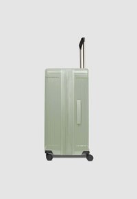 Valise rigide verte avec rainures verticales, poignée rétractable, quatre roues noires et prise latérale. Design durable et léger.