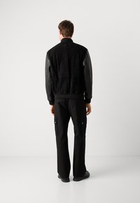 Black bomber jacket with suede body and leather sleeves, ribbed collar and cuffs. Paired with black cargo pants, flat shoes, and minimal design.
