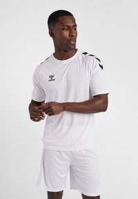 T-shirt et shorts de sport blancs en matériau léger ; présentent un logo Hummel noir et des accents en chevrons noirs sur l'épaule.