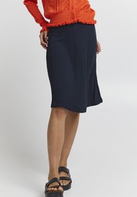 Laivastonsininen ribbihame, jonka pituus on polveen ja lievästi levenevä helma. Yhdistetty mustiin tasapohjaisiin sandaaleihin. Kankaan pinta on teksturoitu, jossa on pystysuorat viivat.