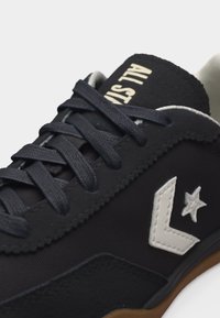 Μαύρο αθλητικό παπούτσι με μαύρα κορδόνια, λευκό λογότυπο σχήματος βέλους και αστέρι στο πλάι, και κείμενο "ALL STAR" στη μαύρη γλώσσα, σε λευκό φόντο.