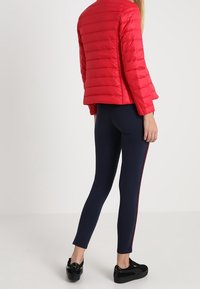 Červená péřová bunda s vodorovným prošíváním, kombinovaná s námořnickými legínami se červeným bočním pruhem; černé platformové boty. Elegantní a přiléhavý design.