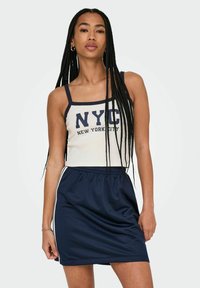 Top in crema con bordini blu navy e testo "NYC"; abbinato a una gonna sportiva blu navy con elastico in vita e strisce laterali.