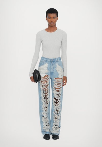 Jeans de lavagem azul clara, desgastados, com grandes remendos rasgados, combinados com uma blusa cinza de mangas longas e uma clutch preta. Tecido liso com detalhes desfiados.