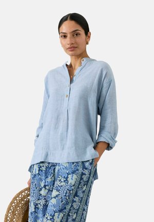 Light blue linen blouse with a buttoned placket and long sleeves, paired with patterned blue trousers featuring floral and stripe designs.