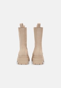 Beige Stiefeletten mit einem eleganten Design, strukturiertem Leder, verstärkten Rückenzügen und einer dicken, robusten Sohle.