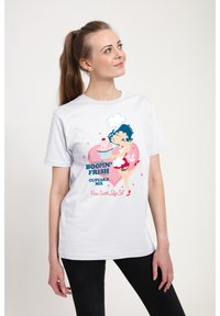 Hvid bomulds t-shirt med et farverigt grafisk motiv af en tegneseriefigur med blåt hår og en pink cupcake, sat mod en baggrund med hjerter.