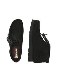 Svarta mockaskor med rund tå och låg profil. Har en flexibel gummisula, dekorativa snören och stickade detaljer längs kanten.