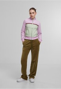 Veste en vert menthe et lavande, zippée avec un col haut et une bande contrastante en marron. Pantalon en velours brun, coupe décontractée. Baskets blanches.