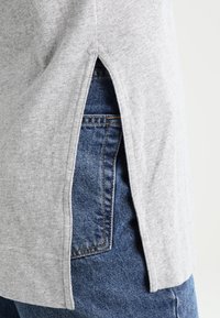 Grå bomullströja med sidofickor, tillsammans med blå denimjeans. Tyget är mjukt med en lätt textur, vilket betonar den avslappnade stilen.