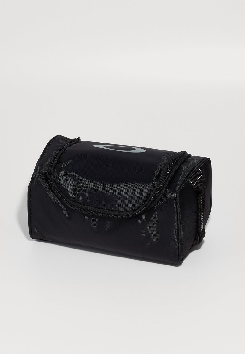 Schwarze Stofftasche mit zylindrischer Form, ausgestattet mit einem glatten Reißverschluss und einem auffälligen grauen Logo auf der Vorderseite. Robustes Material und kompaktes Design.